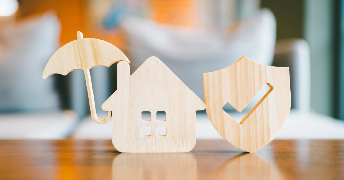 A wooden icon of a home beside an umbrella and a shield