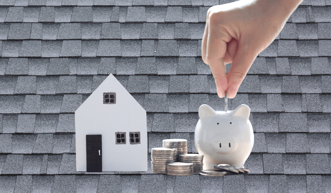 A piggy bank, stack on coins, and home on a background of asphalt shingles